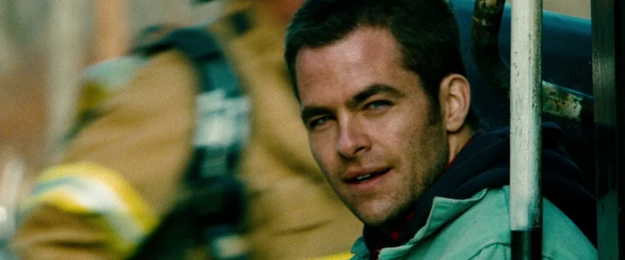 Unstoppable (2010) movie still: closeup — A man sits inside a vehicle while a person in tan gear is blurred nearby. The man gazes toward the camera…