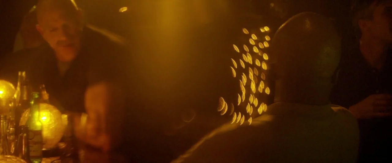 Officer Downe (2016) movie still: medium — A dimly lit bar at night with glowing spherical lamps on the counter surface. Two men sit at the bar…