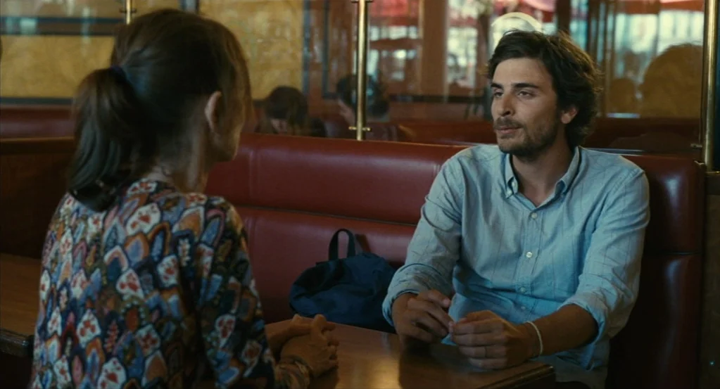 Things to Come (2016) movie still: medium — A red vinyl diner booth sits in a dimly lit establishment with wood paneling. A man sits facing the…