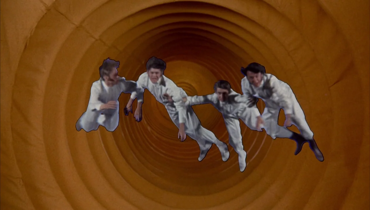 Head (1968) movie still: wide — Four men in white outfits float against a textured, concentric orange tunnel background. The subjects appear…