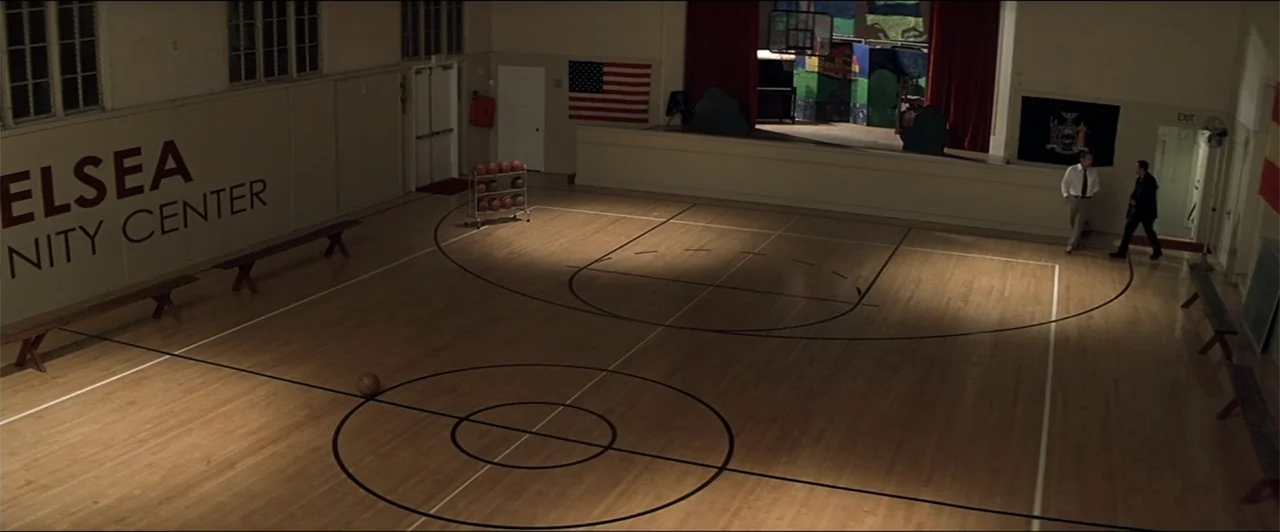 Anger Management (2003) movie still: wide — A spacious high school basketball court features wooden floors, wall-mounted benches, and a small stage.…