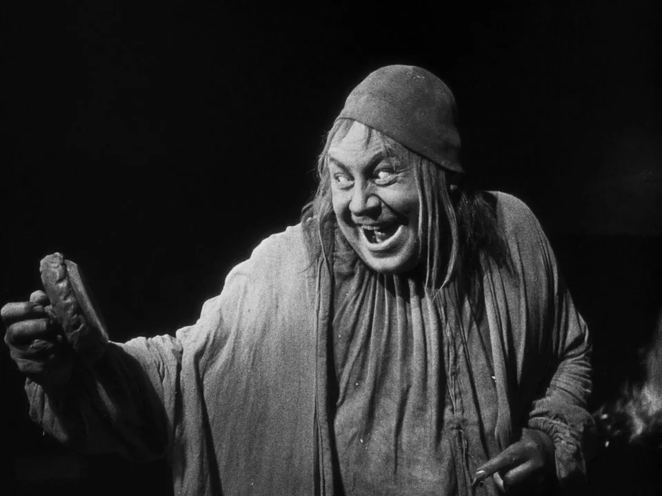 Faust (1926) movie still: medium — A dimly lit dark interior against a black background with no visible architecture. A man in a period tunic…