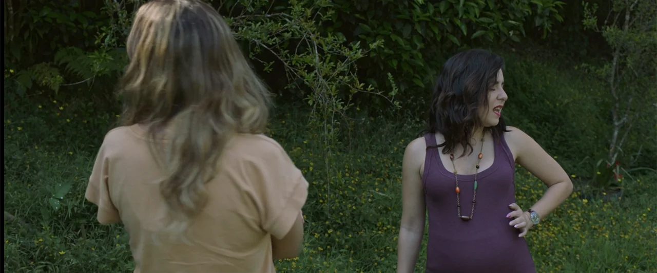 Mirreyes contra Godínez 2: El retiro (2022) movie still: medium — A woman stands in a green field of wildflowers near dense bushes. She engages in…