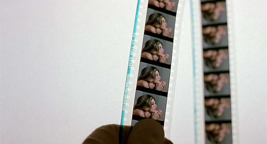 CQ (2001) movie still: closeup — Two strips of processed color film are held up against a bright white light table. Each frame of the film contains…
