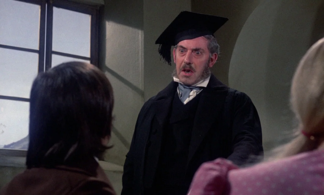 The Horror of Frankenstein (1970) movie still: medium — An academic man stands in a room with a window featuring simple frames. The man wears an…