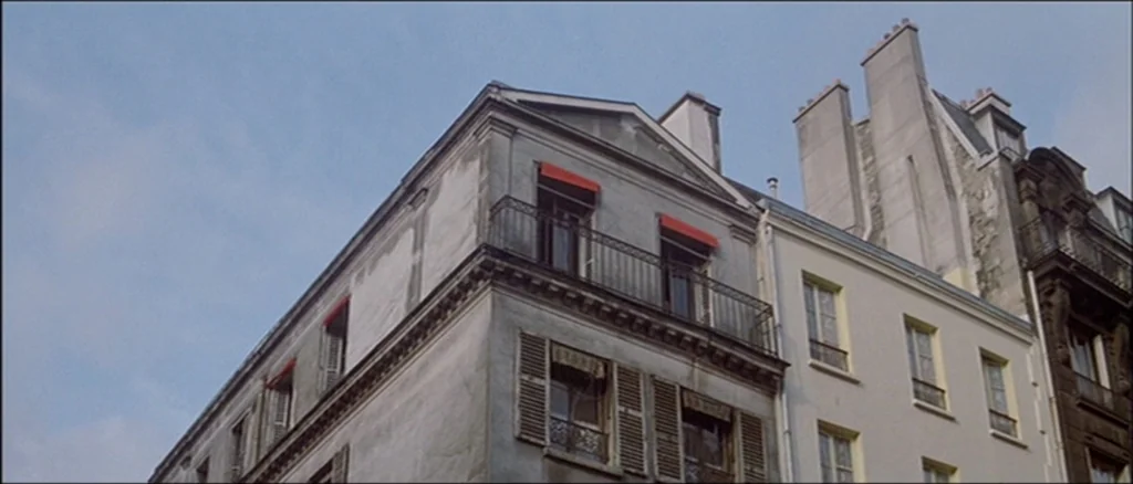 Une Femme Est Une Femme (A Woman Is a Woman) (1961) movie still: establishing — A corner view of multi-story European townhouses features weathered…