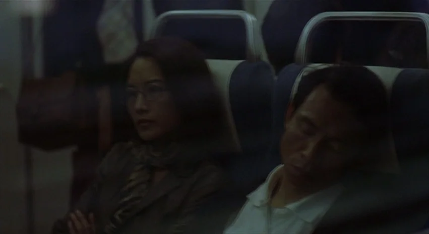 Yi-Yi (A One and A Two) (2000) movie still: medium — An dimly lit airplane cabin features passengers seated in rows of blue seats. A woman sits…