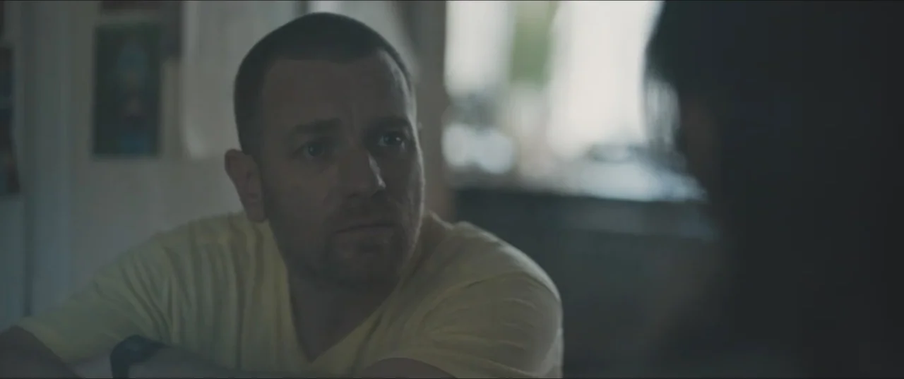 Zoe (2018) movie still: closeup — An interior kitchen setting shows a man sitting and listening to an unseen person. Soft natural light illuminates…