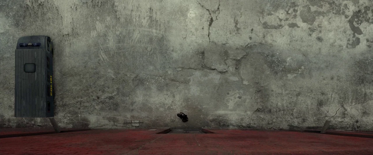 The Raid 2 (2014) movie still: wide — An alleyway features a tall, weathered concrete wall above a red brick foundation. A police van is parked on…