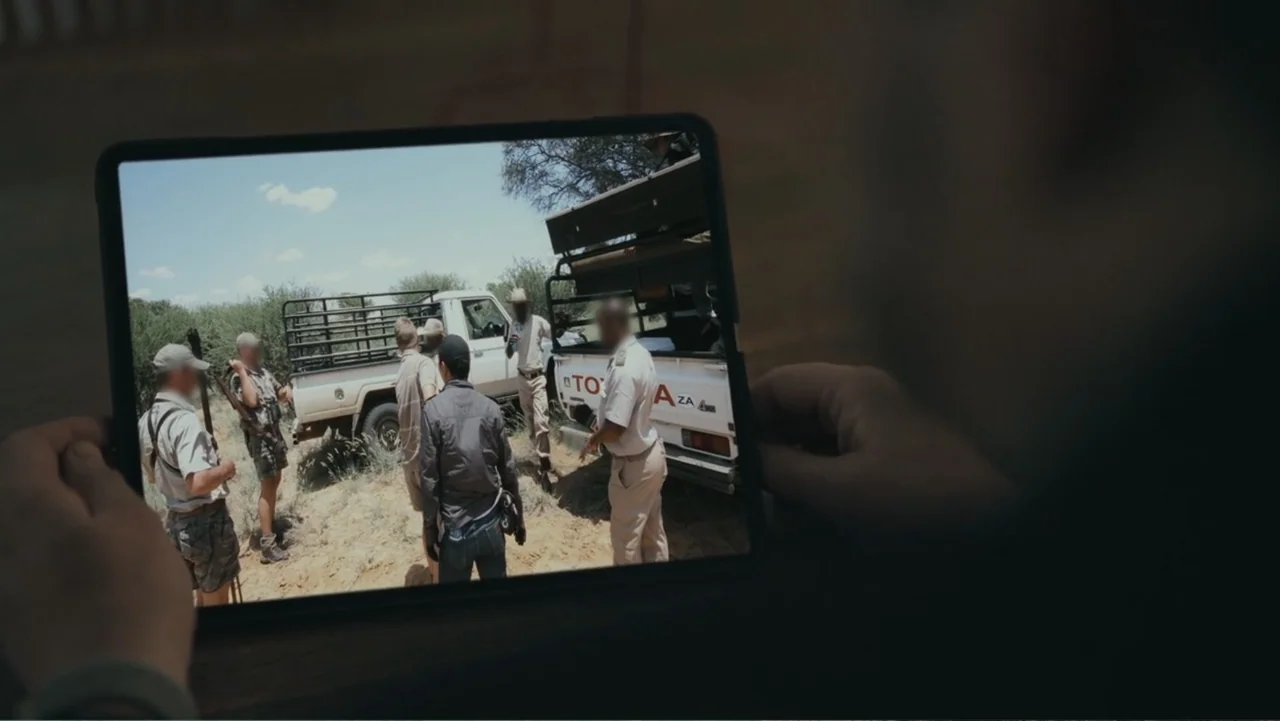 Bloody Trophy (2025) movie still: closeup — A group of five individuals stands in a dry, sparse field next to two trucks. They are engaged in…