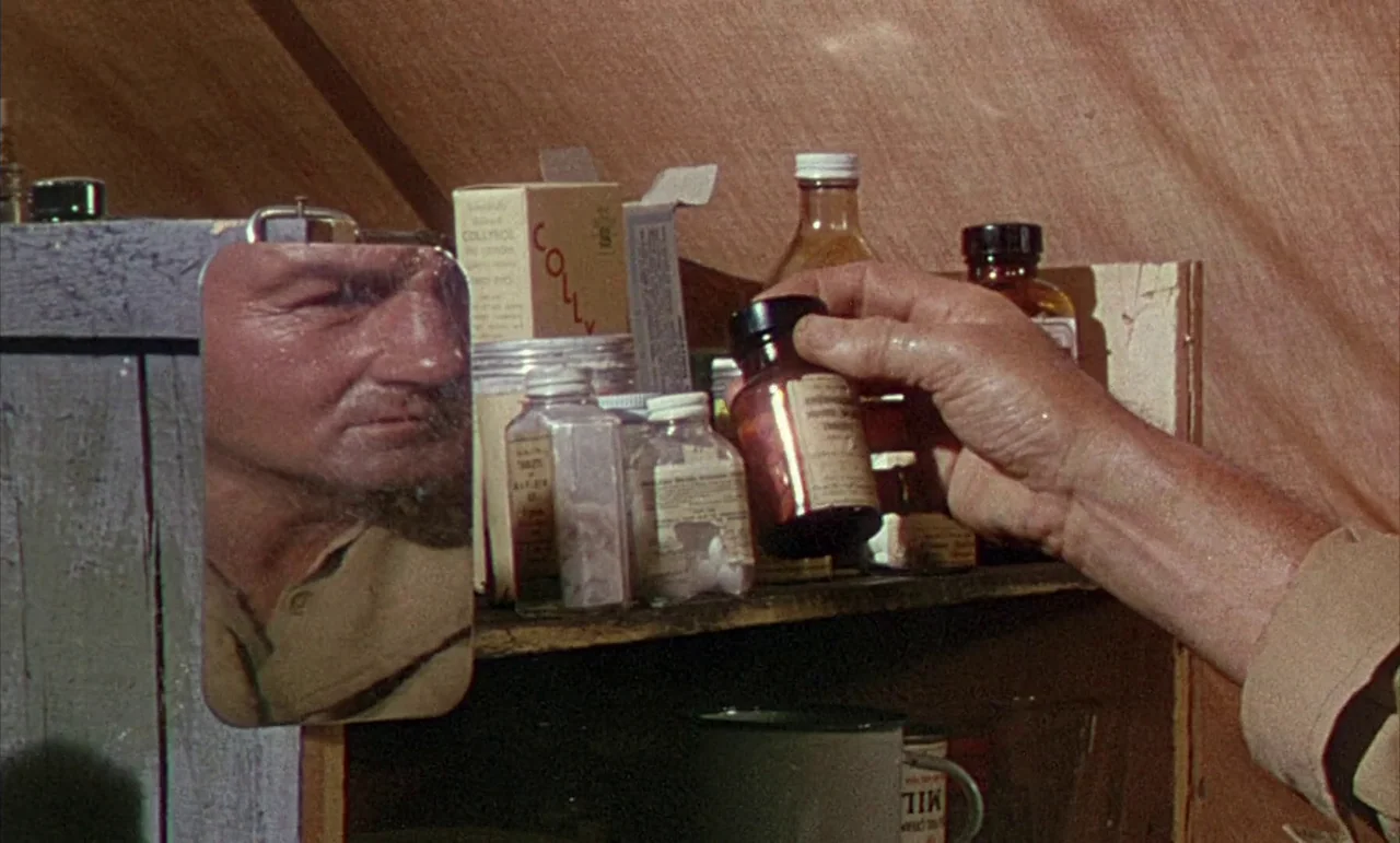 The Purple Plain (1954) movie still: closeup — A wooden shelf inside a canvas tent holds various medicine bottles and paper boxes. A man looks at…