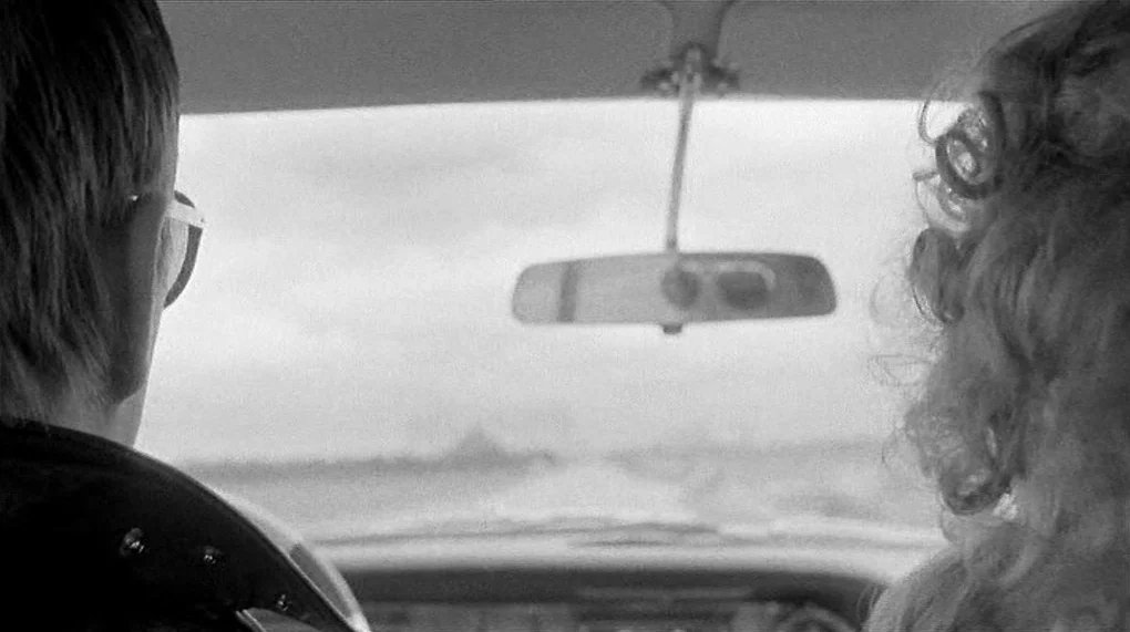 Love Is Colder Than Death (1969) movie still: medium — The interior of a vehicle seen from the perspective of the back seat. A man and a woman sit…