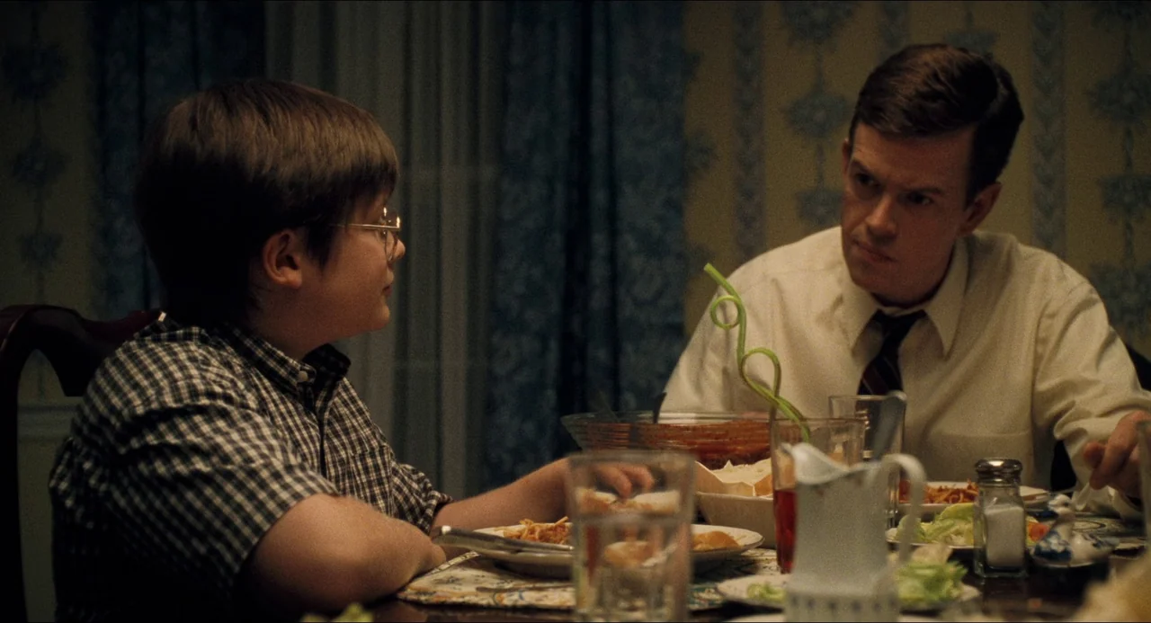 Happiness (1998) movie still: medium — A dimly lit dining room with floral wallpaper and blue curtains. A child and man eat dinner together at a…