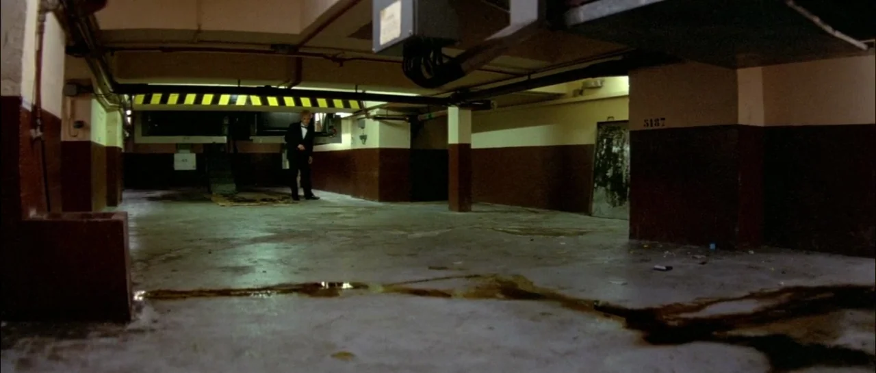 Subway (1985) movie still: wide — An underground concrete parking structure features dark brown lower walls and overhead ventilation ducts. A lone…
