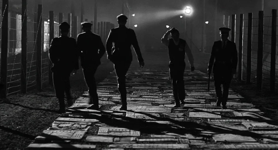 Schindler's List (1993) movie still: wide — A dark night at a cemetery where old stone tombstones pave the walking path. Five men in dark period…