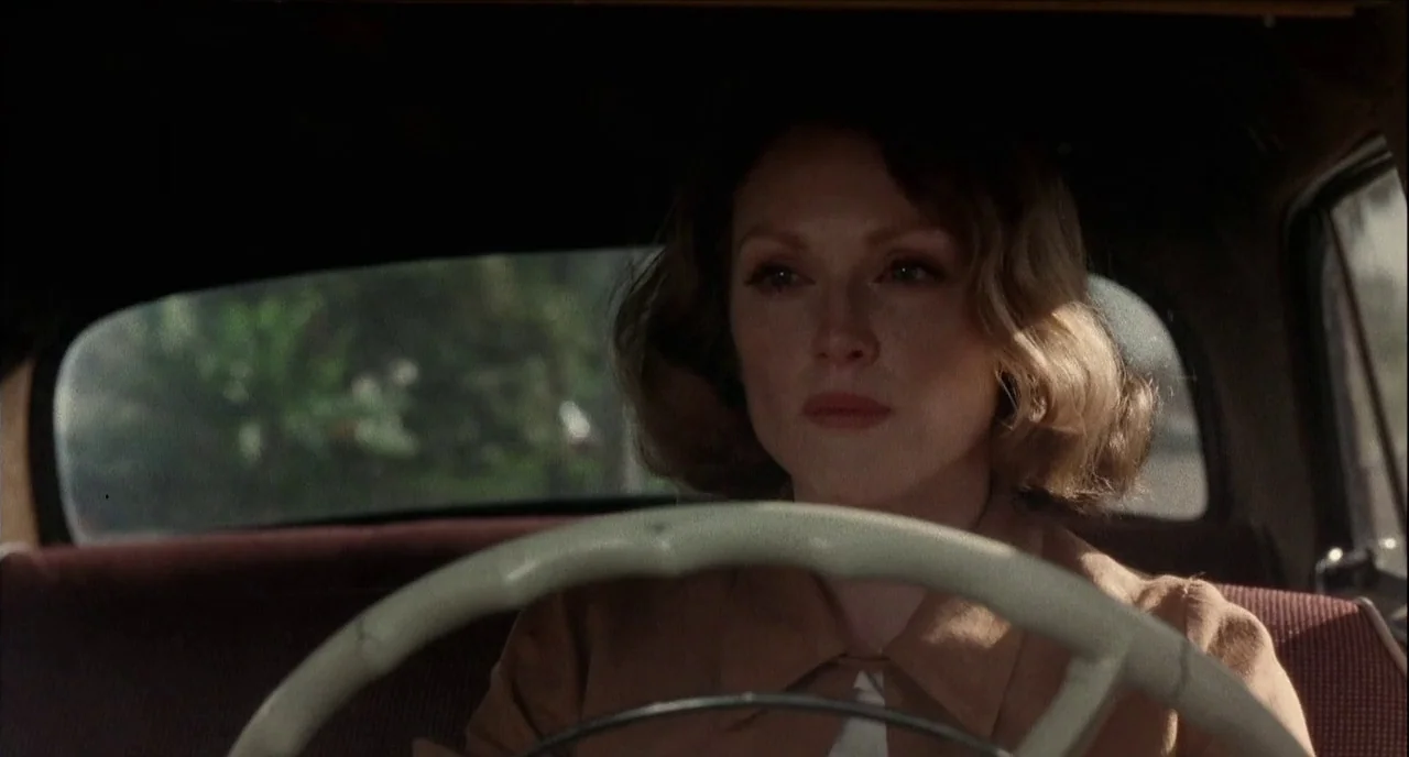The Hours (2002) movie still: medium — The interior of a vintage automobile during the day with blurred greenery visible outside. A woman with wavy…