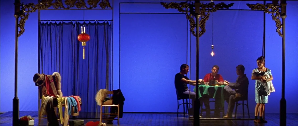 All About My Mother (1999) movie still: wide — A theatrical set features metal frames against an intense, solid blue backdrop. Three men sit at a…