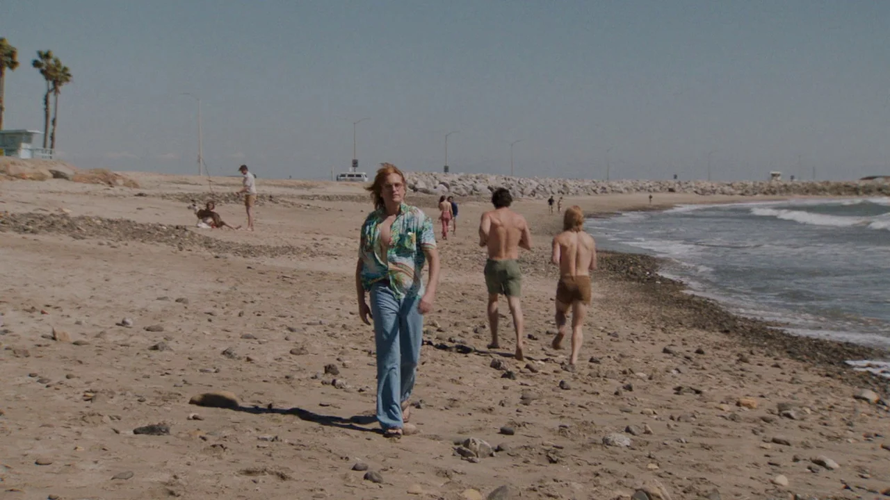 Don't Worry, He Won't Get Far on Foot (2018) movie still: fullbody — A rocky coastal beach features palm trees and a distant breakwater under clear…