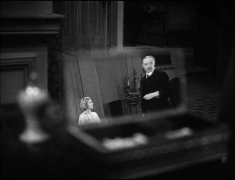 Dracula (1931) movie still: medium — A dimly lit room interior is viewed through a reflection in a small mirror. An older man in a suit stands while…