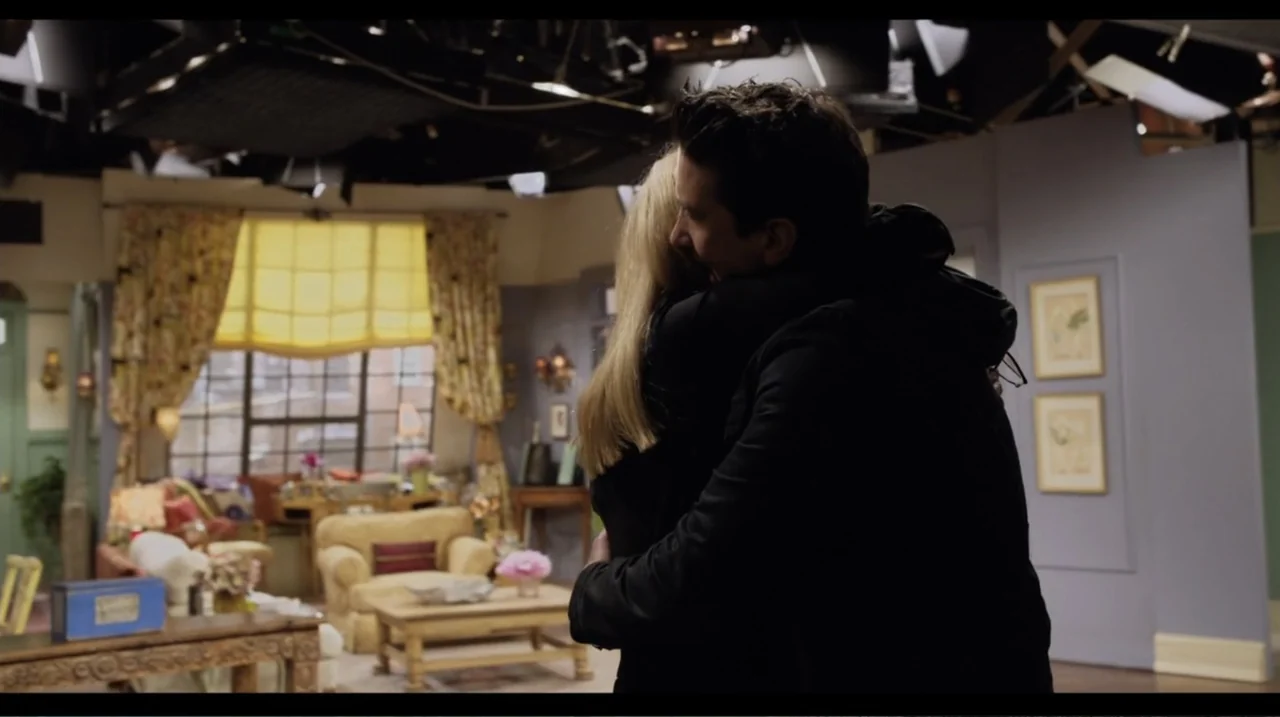 Friends: The Reunion (2021) movie still: medium — A brightly lit television studio set with a living room decor visible in background. A man and a…