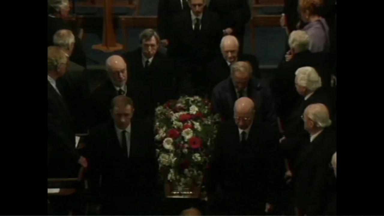 Matthews (2017) movie still: medium — An interior view of a church aisle filled with people in dark funeral attire. A group of men carries a coffin…