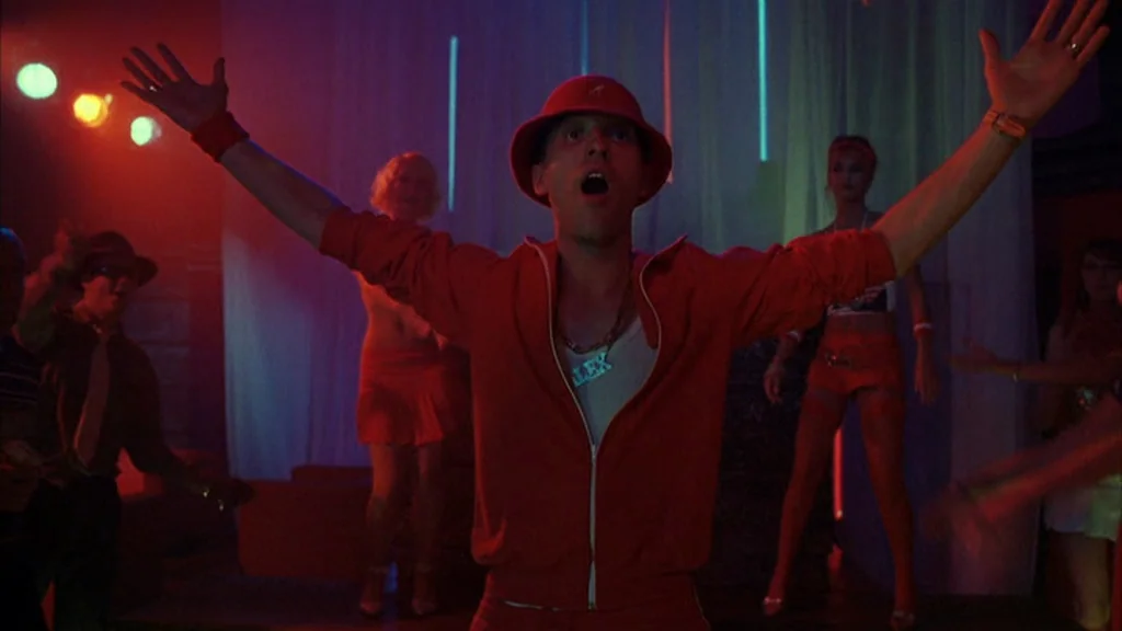Everything Is Illuminated (2005) movie still: medium — A dark, neon-lit nightclub interior with people dancing in the background. A young man in a…