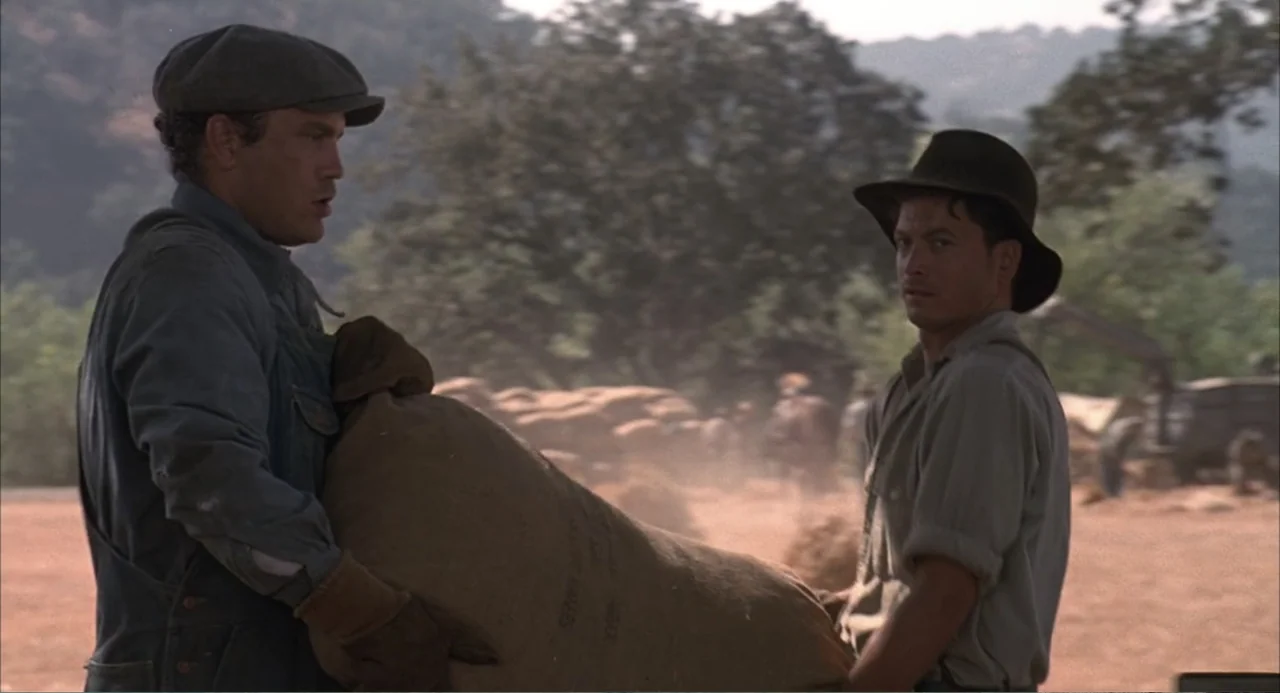 Of Mice and Men (1992) movie still: medium — A sunlit farm field with dry earth and distant trees in the background. Two men in period work clothes…