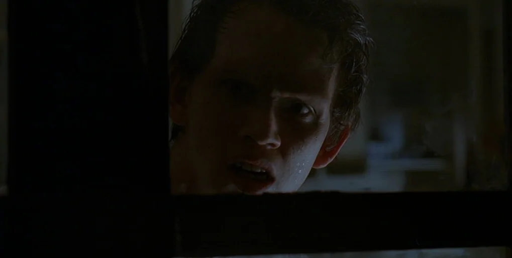 Dominion: Prequel to the Exorcist (2005) movie still: closeup — A man's face appears behind a dark window frame in a nighttime interior setting. He…