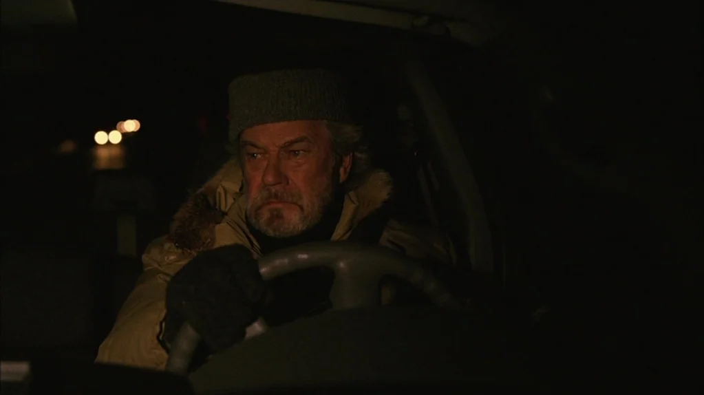 Away From Her (2006) movie still: medium — An older man operates a vehicle interior at night with a dark road ahead. Bright white headlight bokeh…