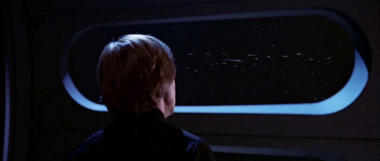 Return Of The Jedi (1983) movie still: medium — A dark, dimly lit cabin features an elongated horizontal window overlooking a vast starfield. A…