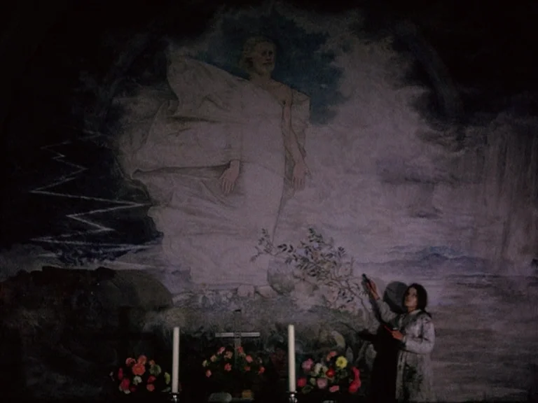 Der Bomberpilot (1970) movie still: wide — A dark church interior features a large wall mural of a robed figure. A woman stands in the foreground,…