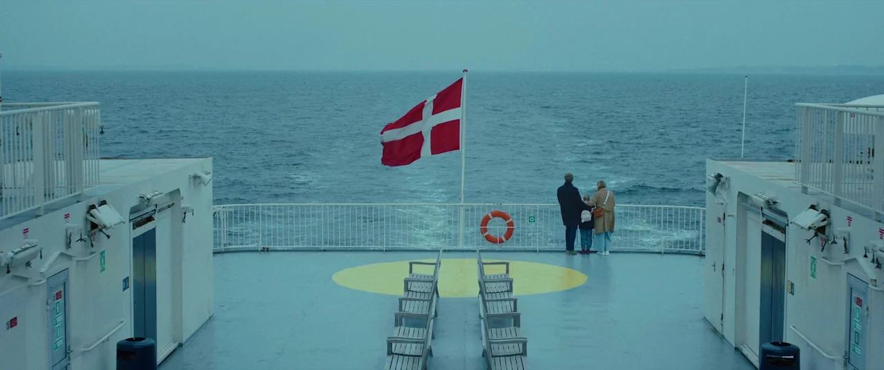 Speak No Evil (2022) movie still: wide — An expansive outdoor ferry deck features metal benches, a yellow circle, and railing. A group of three…