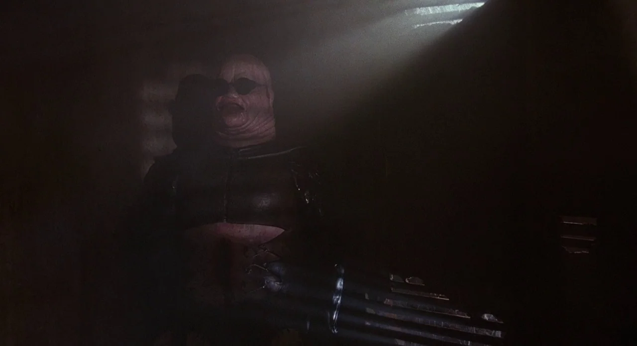 Hellraiser (1987) movie still: medium — A dark, enclosed space is lit by a single beam of light from above. A monstrous, bald humanoid figure with…
