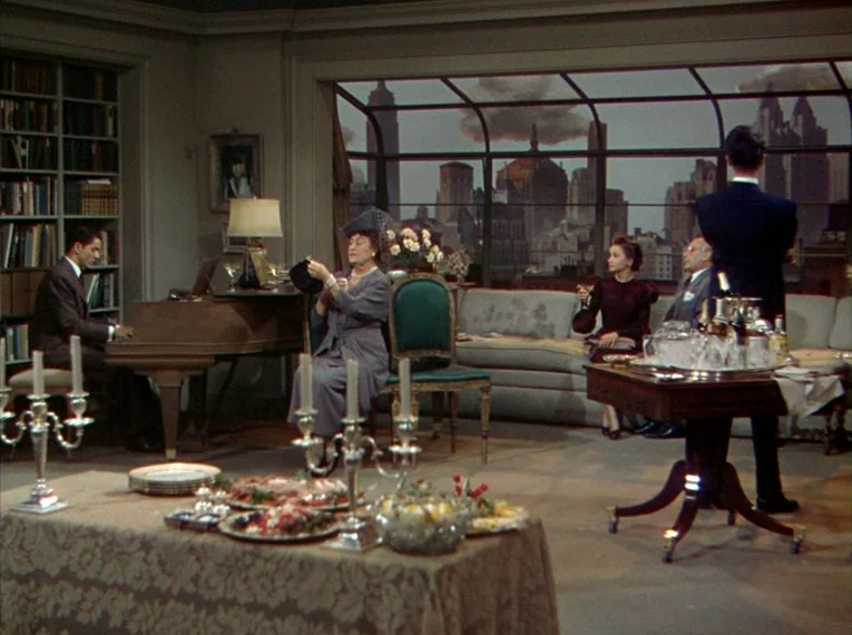 Rope (1948) movie still: wide — A spacious penthouse with floor-to-ceiling windows overlooking a New York skyline at dusk. Guests gather for a…