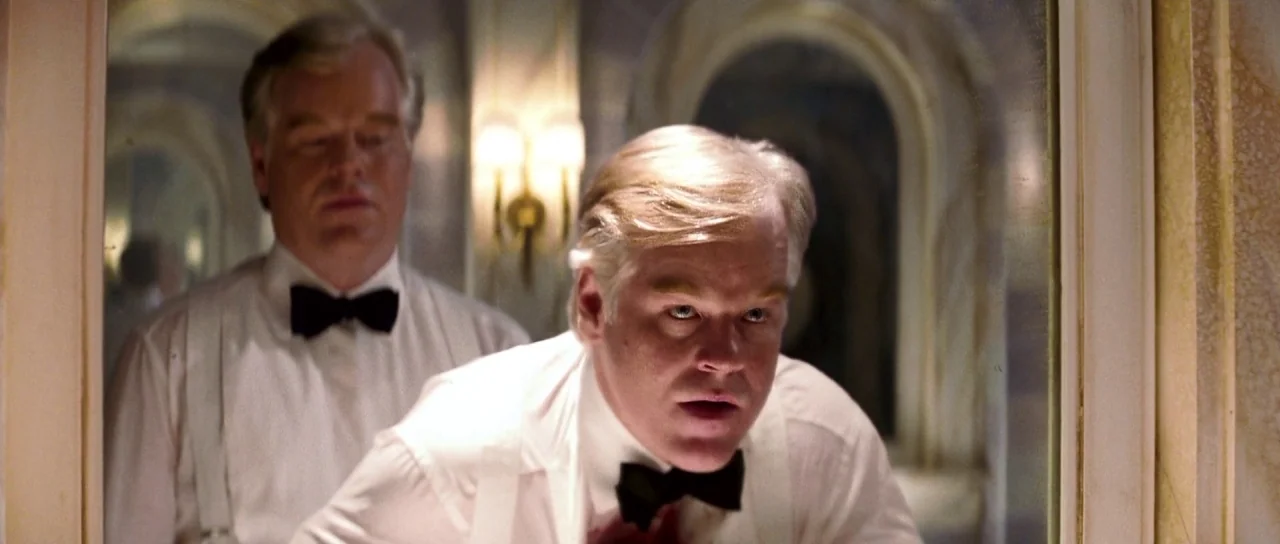 Down With Love (2003) movie still: medium — A tiled bathroom with an arched wall-mounted mirror displaying a reflection of two men. Both men are…