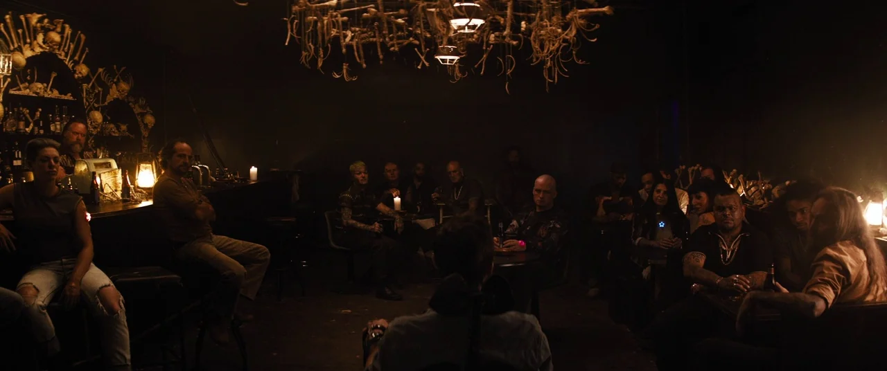Upgrade (2018) movie still: wide — A dimly lit bar is decorated with bone structures hanging from the ceiling. A crowd of people sits in the dark…