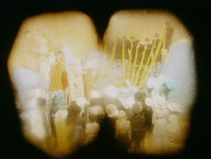 Careful (1992) movie still: wide — An outdoor area is filled with a large crowd of people in period clothing. The image is viewed through…