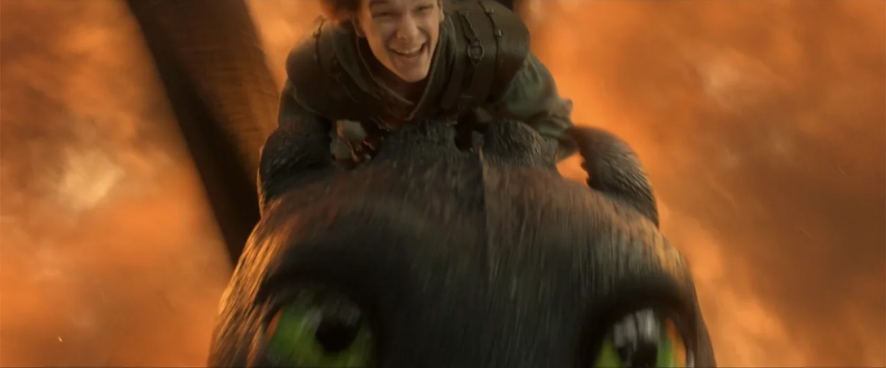 How to Train Your Dragon (2025) movie still: closeup — The scene takes place high in the night sky surrounded by swirling orange embers. A young boy…