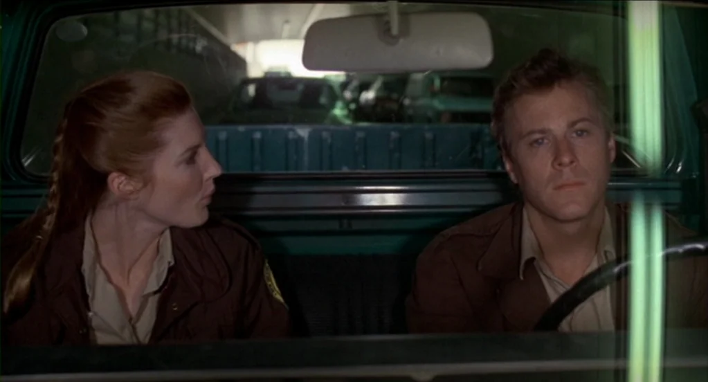 Cat People (1982) movie still: medium — The interior of a teal-colored truck during the day viewed from the exterior windshield. A man drives while…