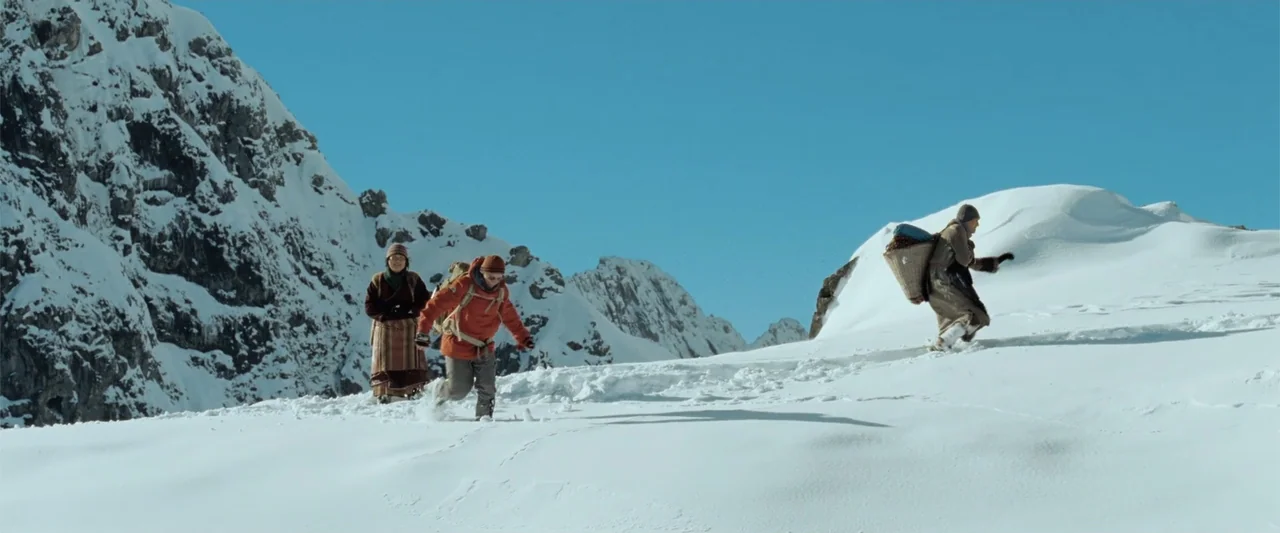 Hector and the Search for Happiness (2014) movie still: wide — Three individuals climb a steep, snow-packed mountain range under a cloudless blue…