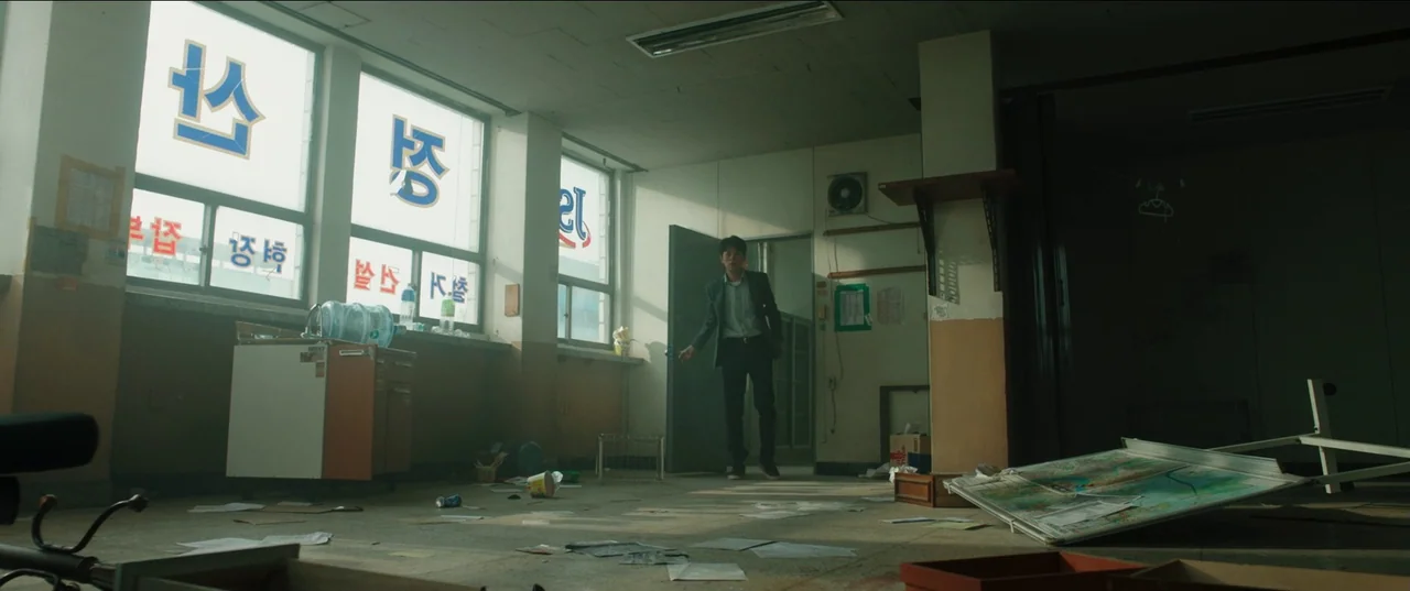 Psychokinesis (2018) movie still: wide — A cluttered, disheveled office space features papers scattered across the dusty floor. A lone man in a suit…