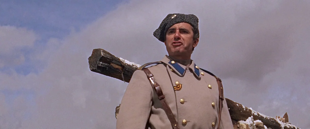 Doctor Zhivago (1965) movie still: medium — An open snowy area with a dark wooden beam in the background. A soldier in a formal military coat stands…