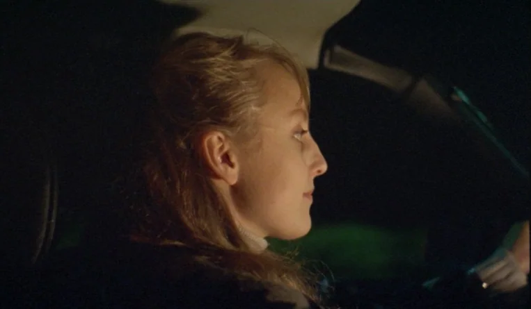 The Turn of the Century (2001) movie still: closeup — A woman driving at night in the interior of an automobile. The frame is dark, focusing on her…