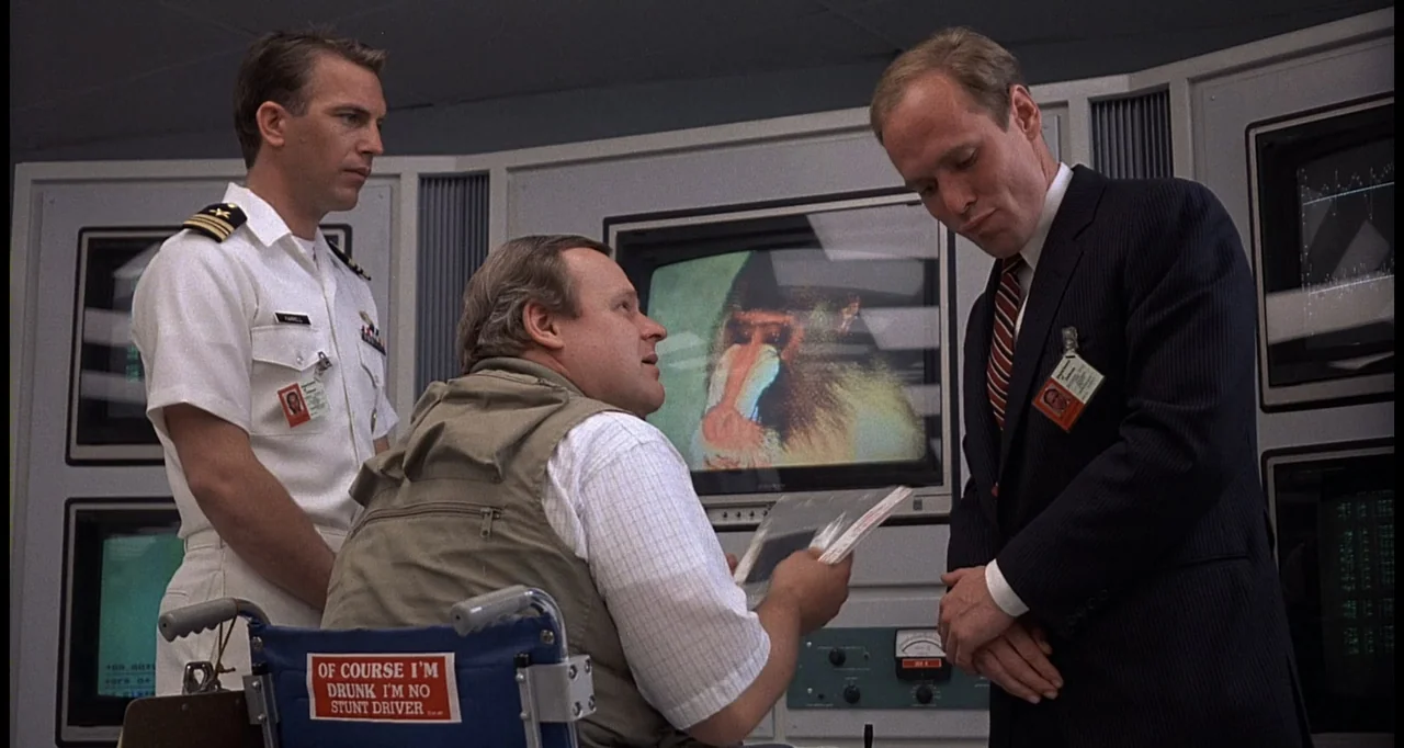 No Way Out (1987) movie still: medium — A high-tech control room features multiple computer terminals displaying imagery of a baboon. Three men…