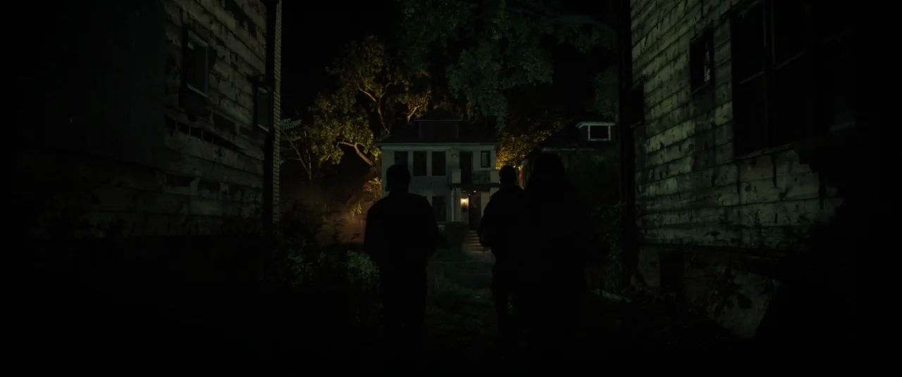 Don’t Breathe (2016) movie still: wide — Two figures walk down a narrow, dark alley between two old weathered houses at night. A lone residential…