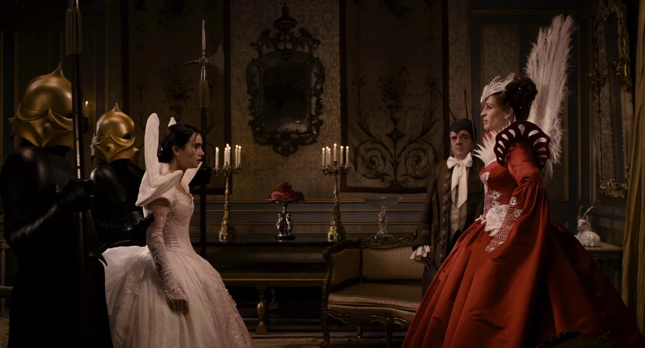 Mirror Mirror (2012) movie still: wide — An opulent, dark room features ornate wallpaper, gold trim, and candelabras on a sideboard. A young woman…