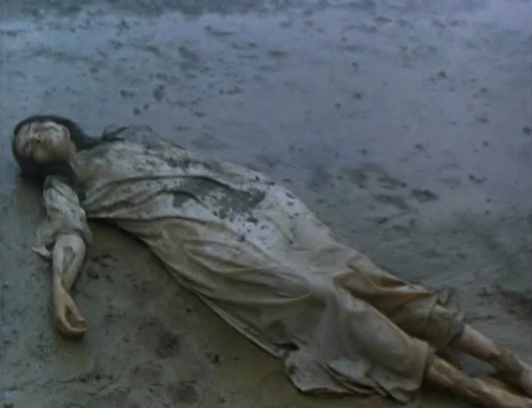 The Wishing Tree (1977) movie still: fullbody — A wet, sandy shoreline stretches under an overcast sky during the daytime. A young woman in a muddy,…