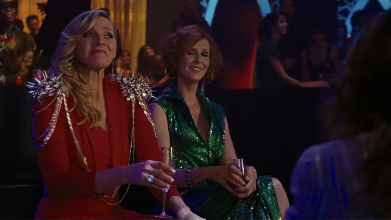 Sex and the City 2 (2010) movie still: medium — A dimly lit club interior features blurred figures in the background. Two women sit at a table…