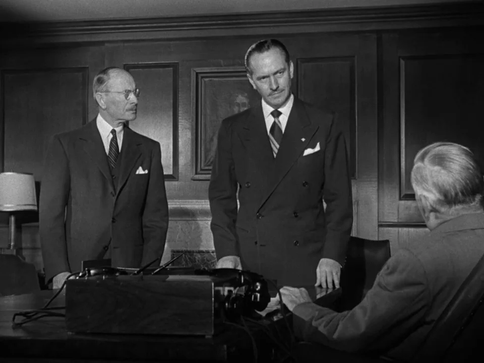 The Best Years of Our Lives (1946) movie still: medium — A paneled wood office with dark walls and a large desk containing audio equipment. Three…