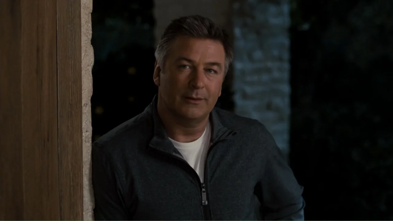 It's Complicated (2009) movie still: medium — A man stands in a shadowed doorway leading to an outdoor stone patio at night. The man leans his…